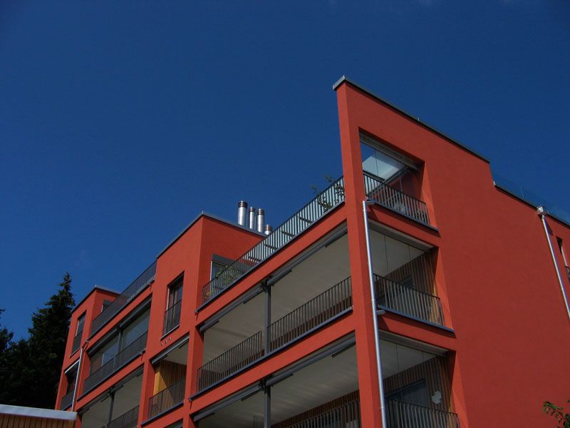 Modernes Mehrfamilienhaus mit orange-roter Fassade vor blauem Himmel