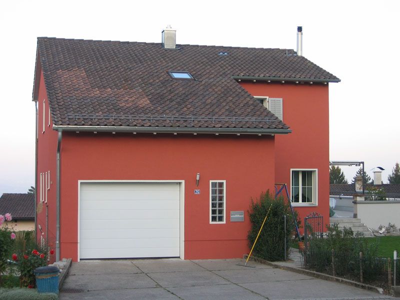Einfamilienhaus mit frisch gestrichener roter Fassade und weissem Garagentor